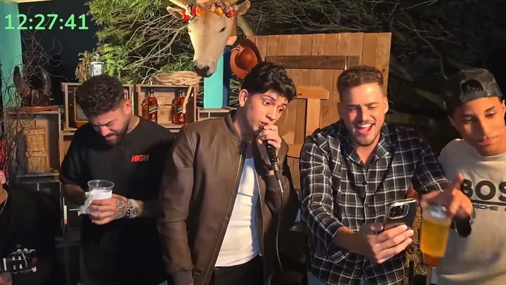 Convidado canta ao microfone enquanto a turma brinda no cenário do bar